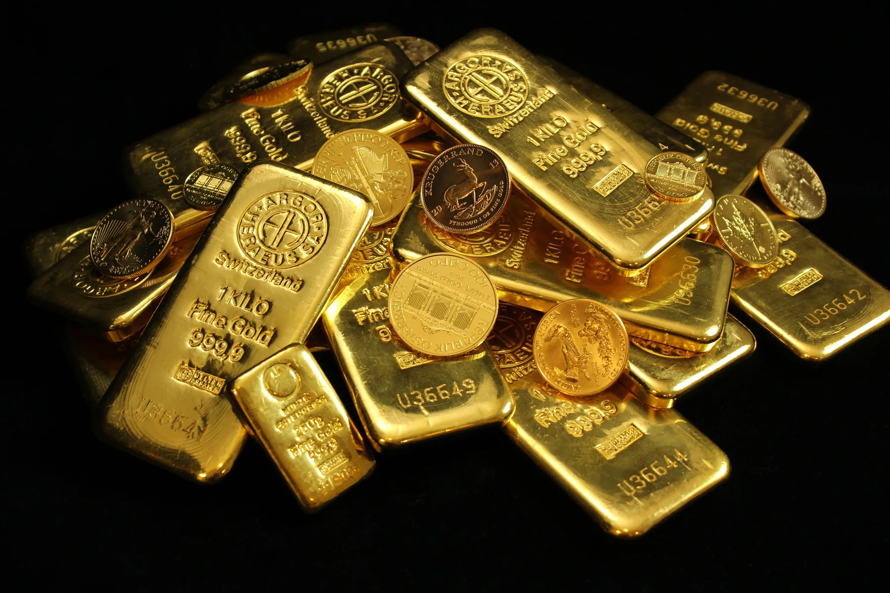 Goldbarren a Mënzen, zesummen op enger donkeler Fläch arrangéiert.