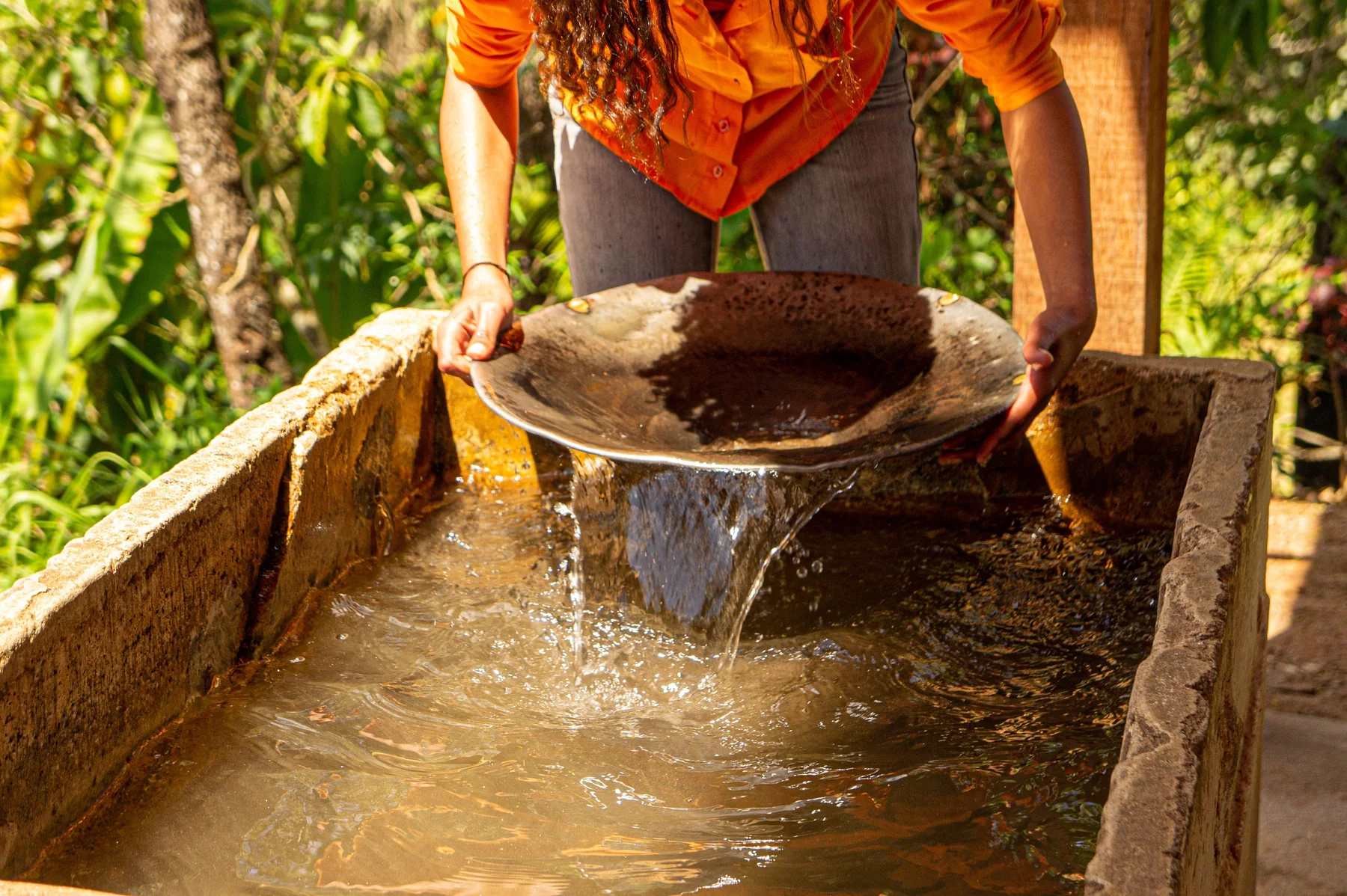 A woman pans sediment through water using a traditional gold-panning method.